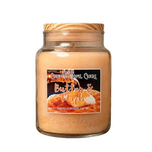 A glass jar candle with a wooden lid, filled with a warm peachy-orange wax. The front features a label that reads 'COUNTRY HOME CANDLE Butters & Maple' with an image of maple syrup dripping over butter.