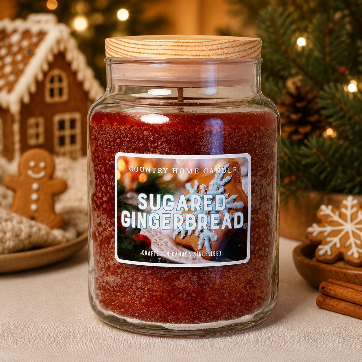 A large glass jar candle labeled 'SUGARED GINGERBREAD' by Country Home Candle, filled with deep red wax and topped with a light wood lid, set on a tabletop with holiday decorations in the background.